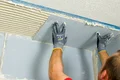 Handwerker montiert Trockenbauplatte an Decke mit Klebemörtel.