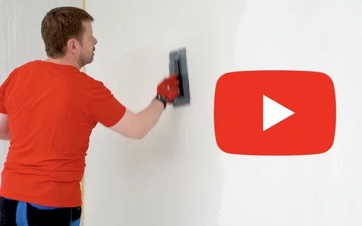 Heimwerker beim Verputzen einer Wand mit Glättkelle, Videoanleitung verfügbar.